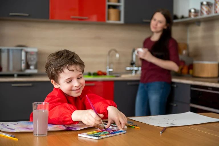 smiling little boy drawing pictures kitchen with mom
